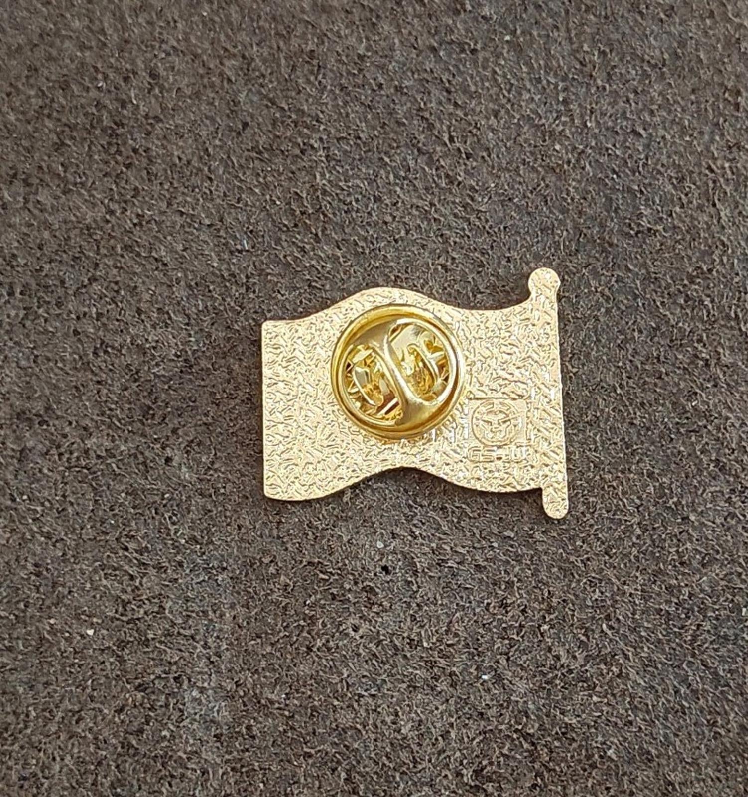 Gold-tone pin back with round raised logo and safety clasp