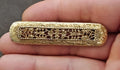 Gold tone Victorian filigree bar brooch close-up with symmetrical openwork and raised details.