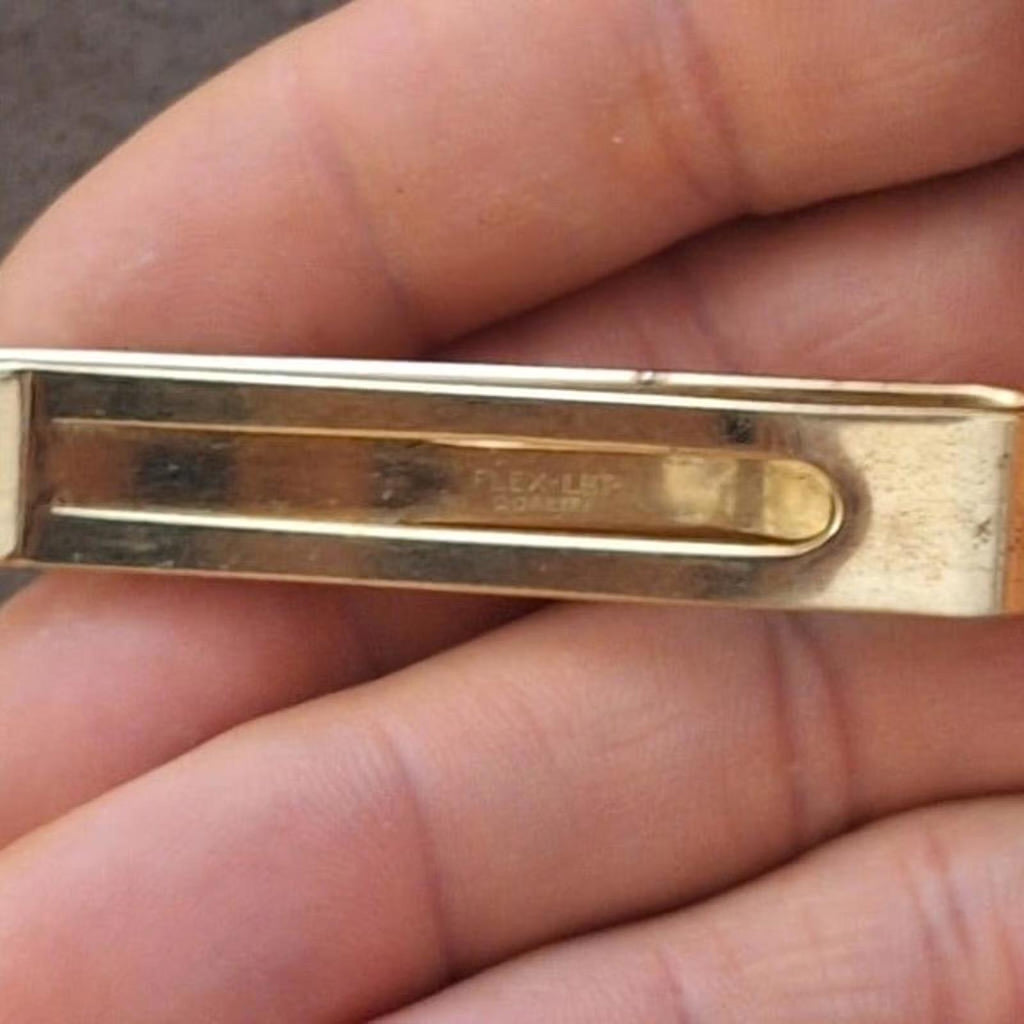Gold tone tie bar clip back with engraved marks on the metal plate