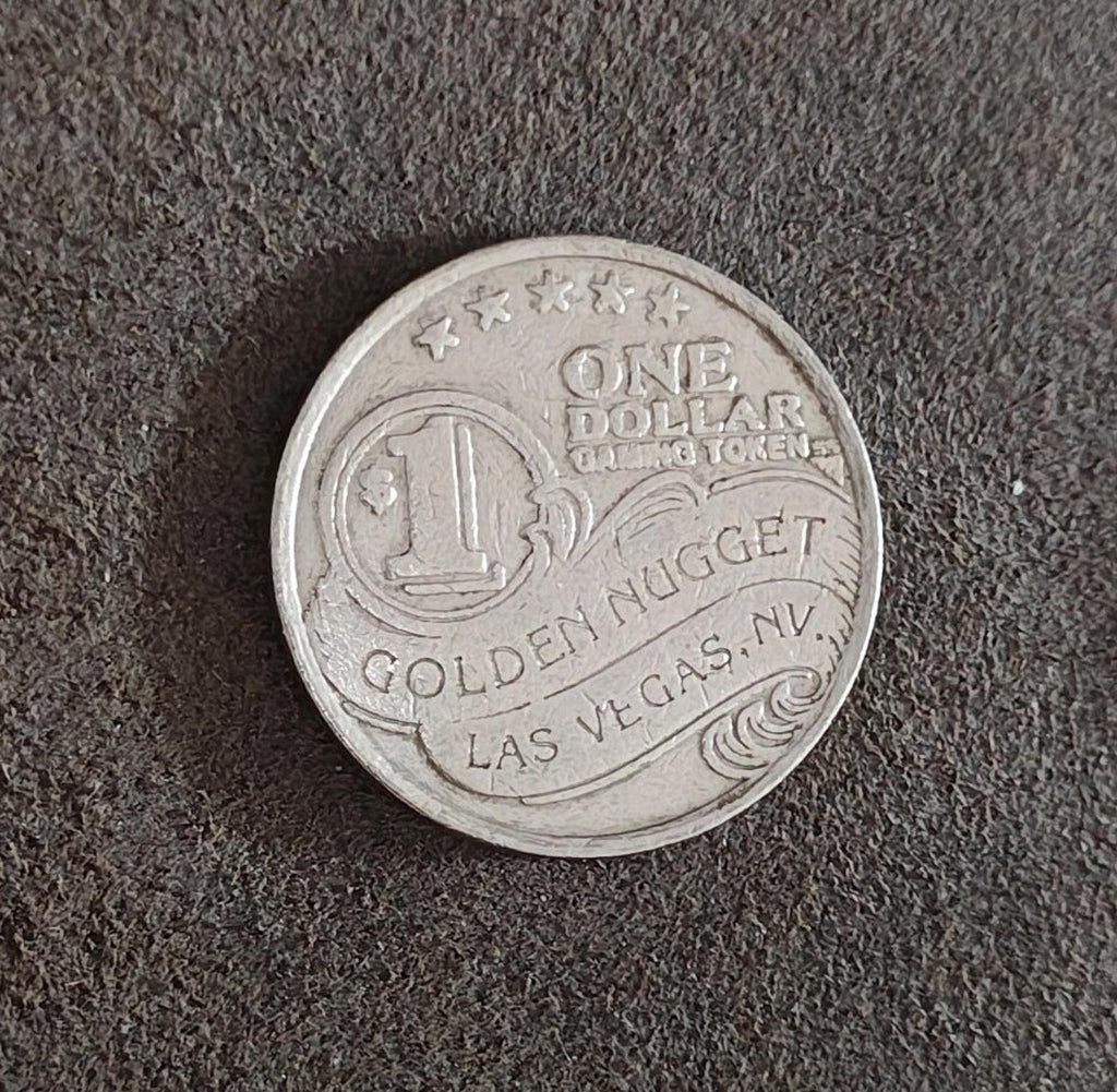 Silver Golden Nugget one-dollar slot token on surface, showing ONE DOLLAR and LAS VEGAS.