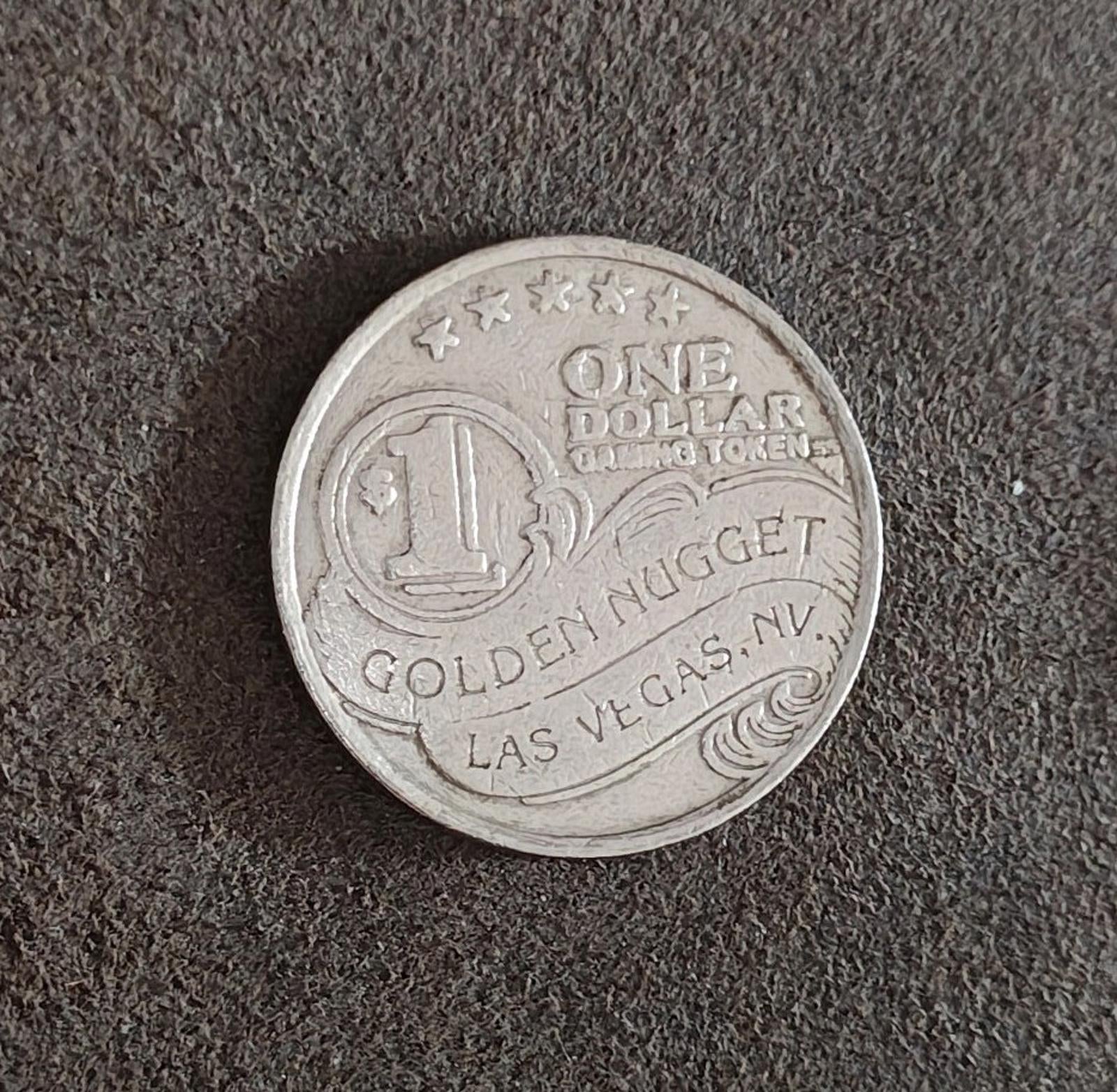 Silver Golden Nugget one-dollar slot token on surface, showing ONE DOLLAR and LAS VEGAS.