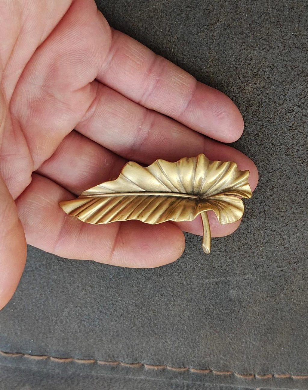 Gold-tone leaf brooch pin with ridged leaf pattern and visible stick pin on back.