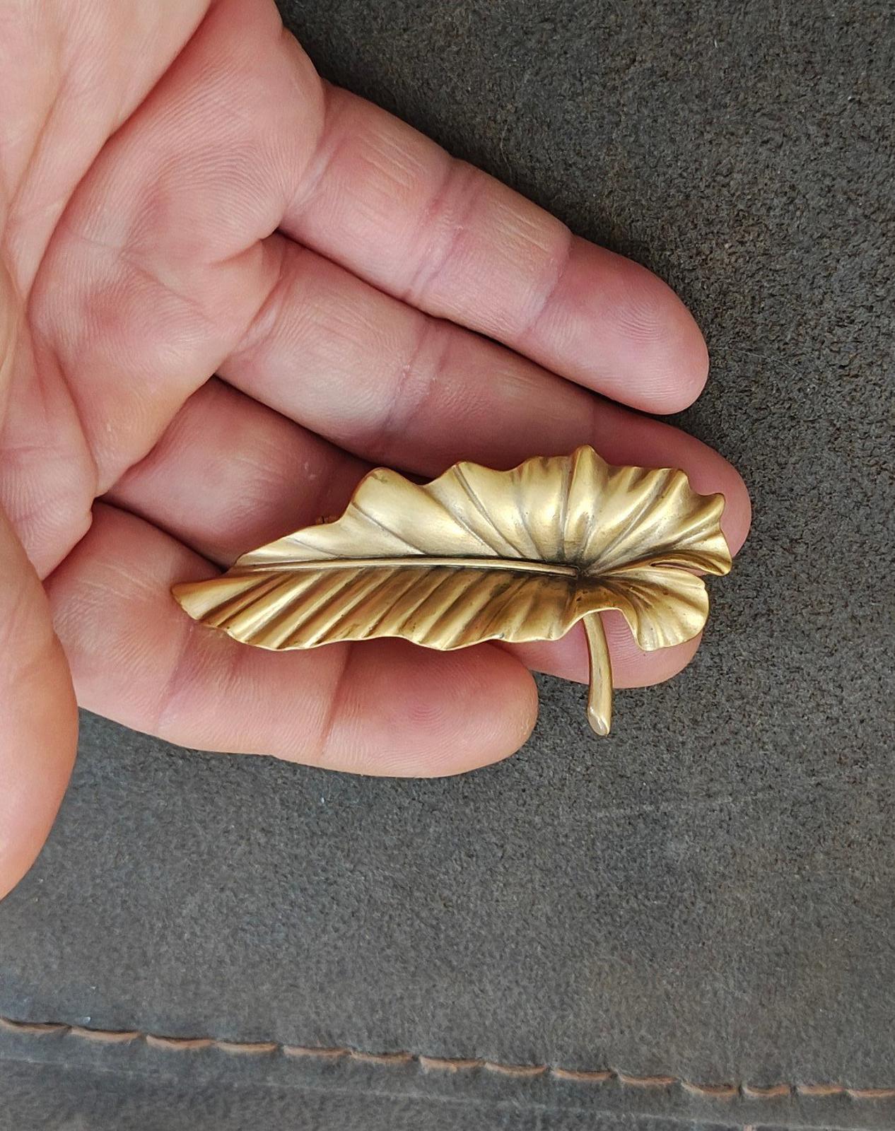 Gold-tone leaf brooch pin with ridged leaf pattern and visible stick pin on back.