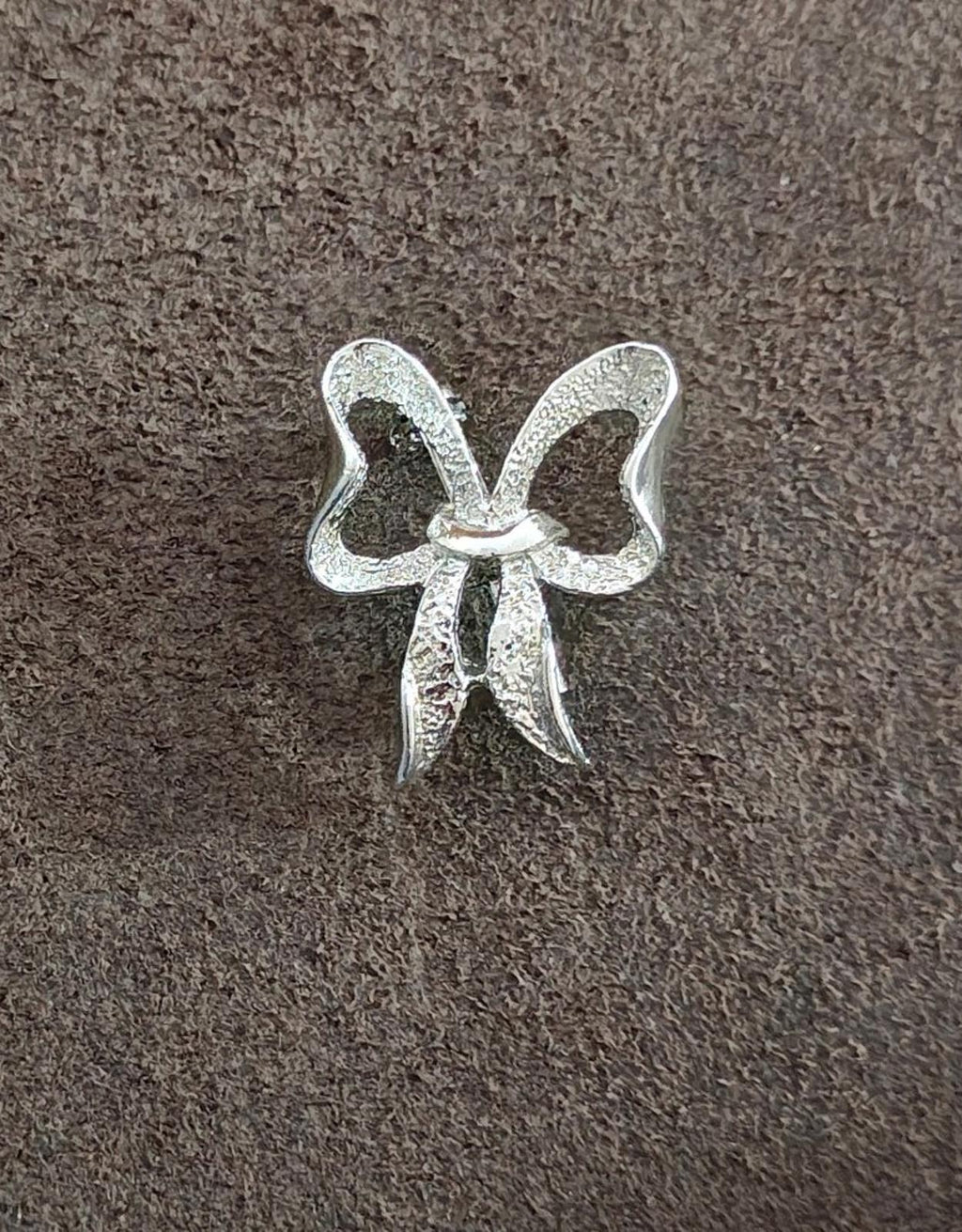 Silver-tone bow brooch pin with textured finish and small knot-like center.