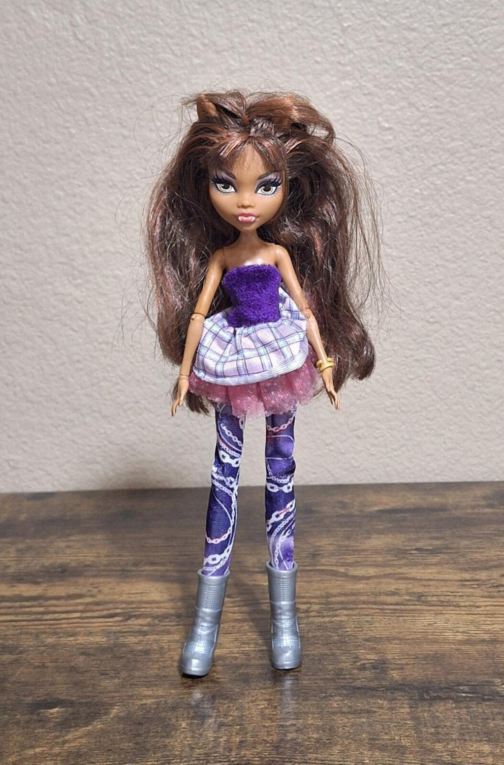 Fashion doll full-body standing with purple glitter top, plaid skirt, and purple leggings