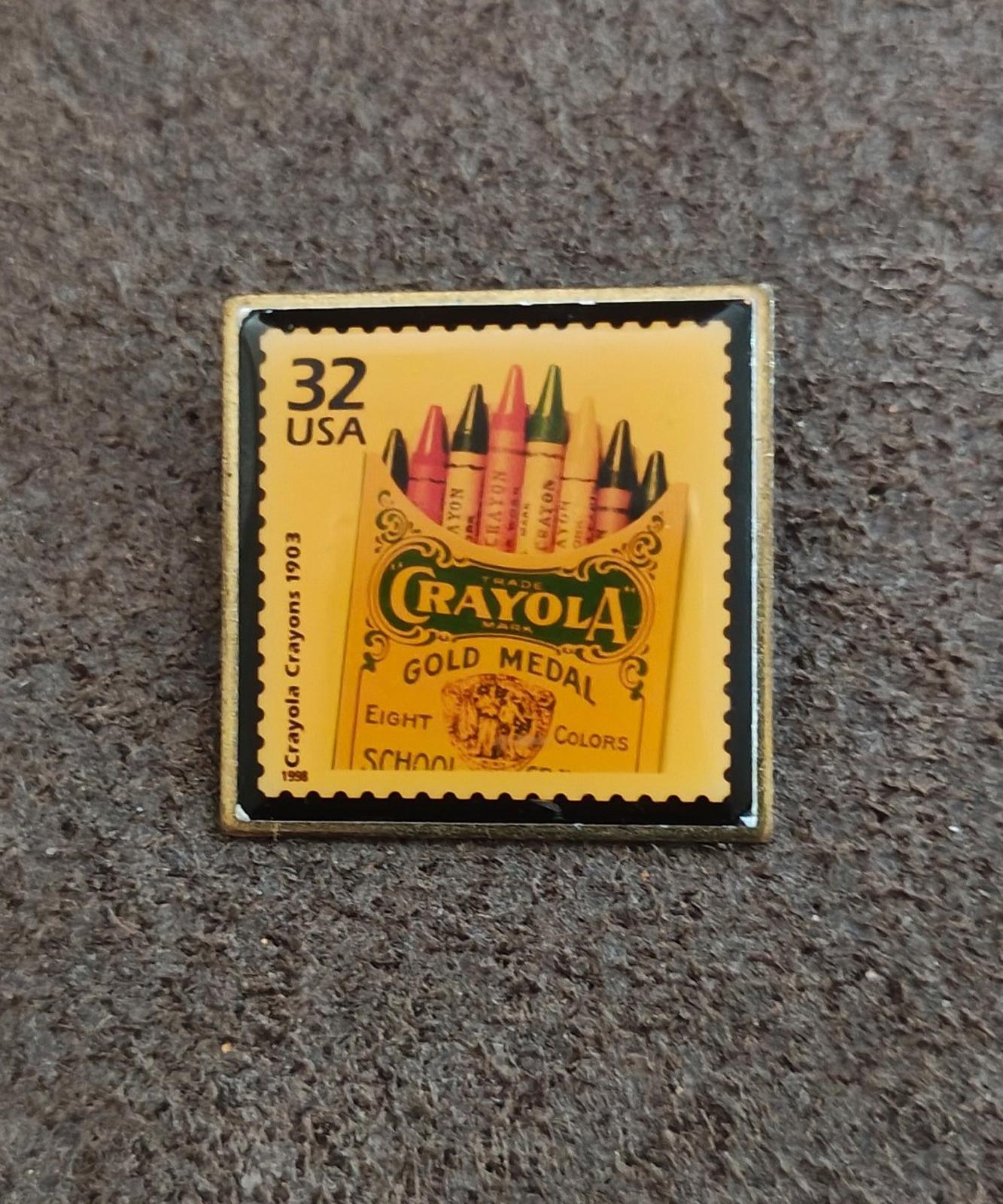 Square gold-tone pin with yellow USPS-style stamp reading “Crayola Gold Medal”