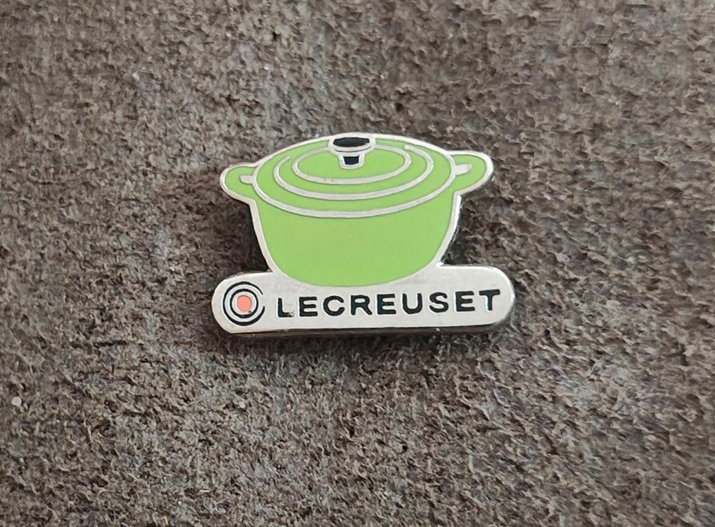 Le Creuset green mini cocotte enamel pin on gray fabric, centered