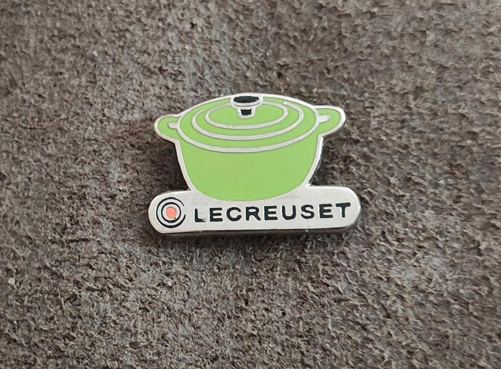 Le Creuset green mini cocotte enamel pin on gray fabric, centered