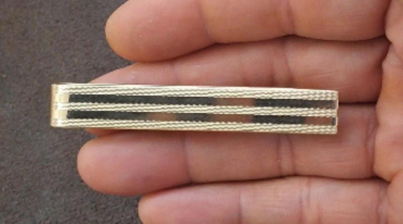 Gold tone tie bar clip with black stripe bands, close-up front view