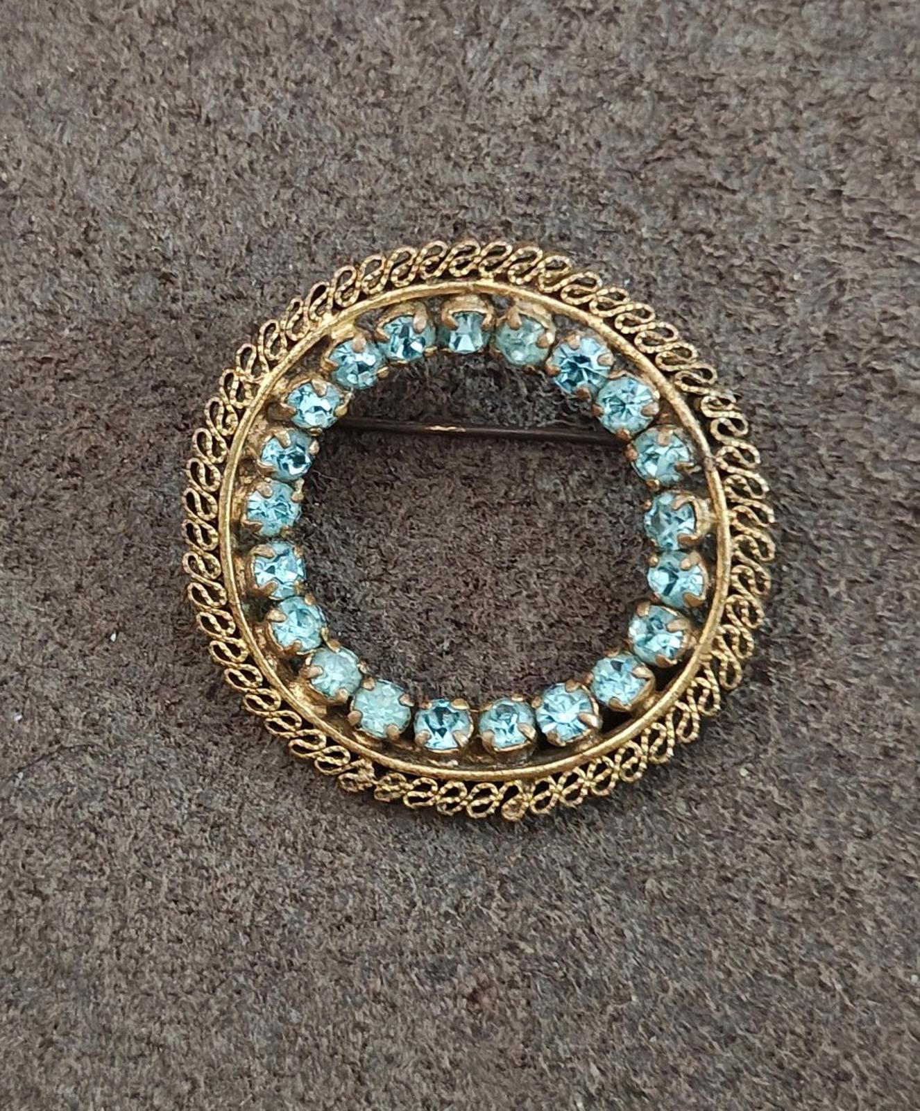 Gold-tone round brooch with blue stone halo and ornate rope-like edge