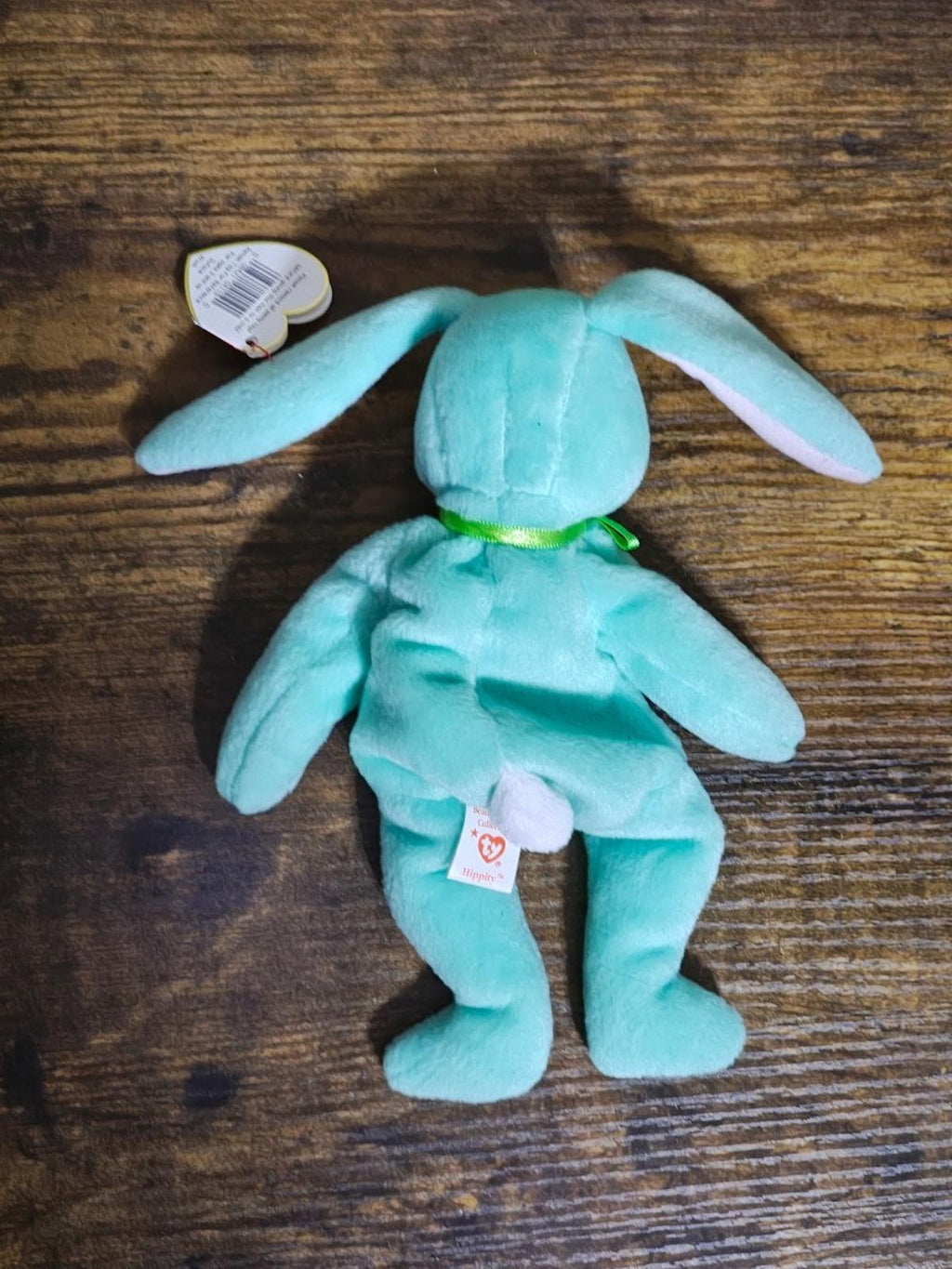 Teal plush bunny beanbag lying on wood with back swing tag visible