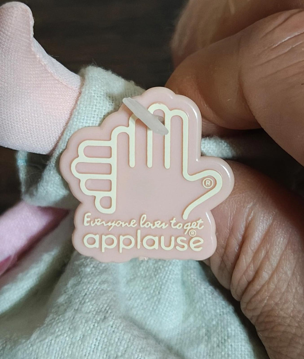 Pink and white appAlause logo tag on mint plush fabric, close-up