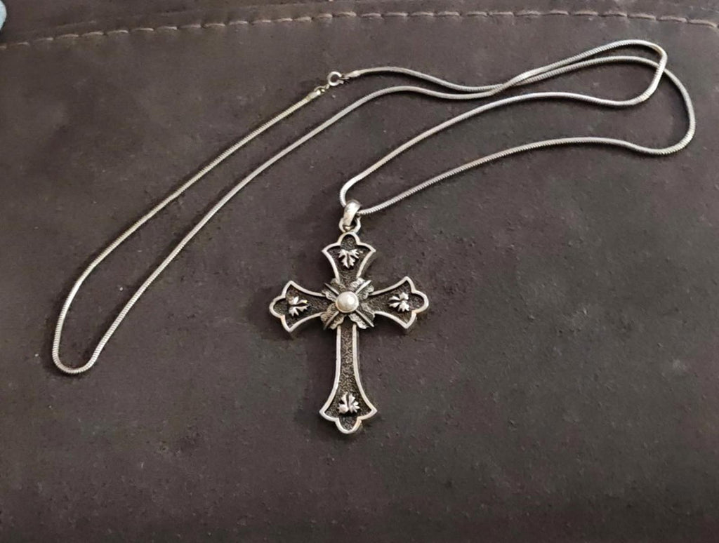 Silver tone cross pendant necklace laid out with adjustable chain and faux pearl center