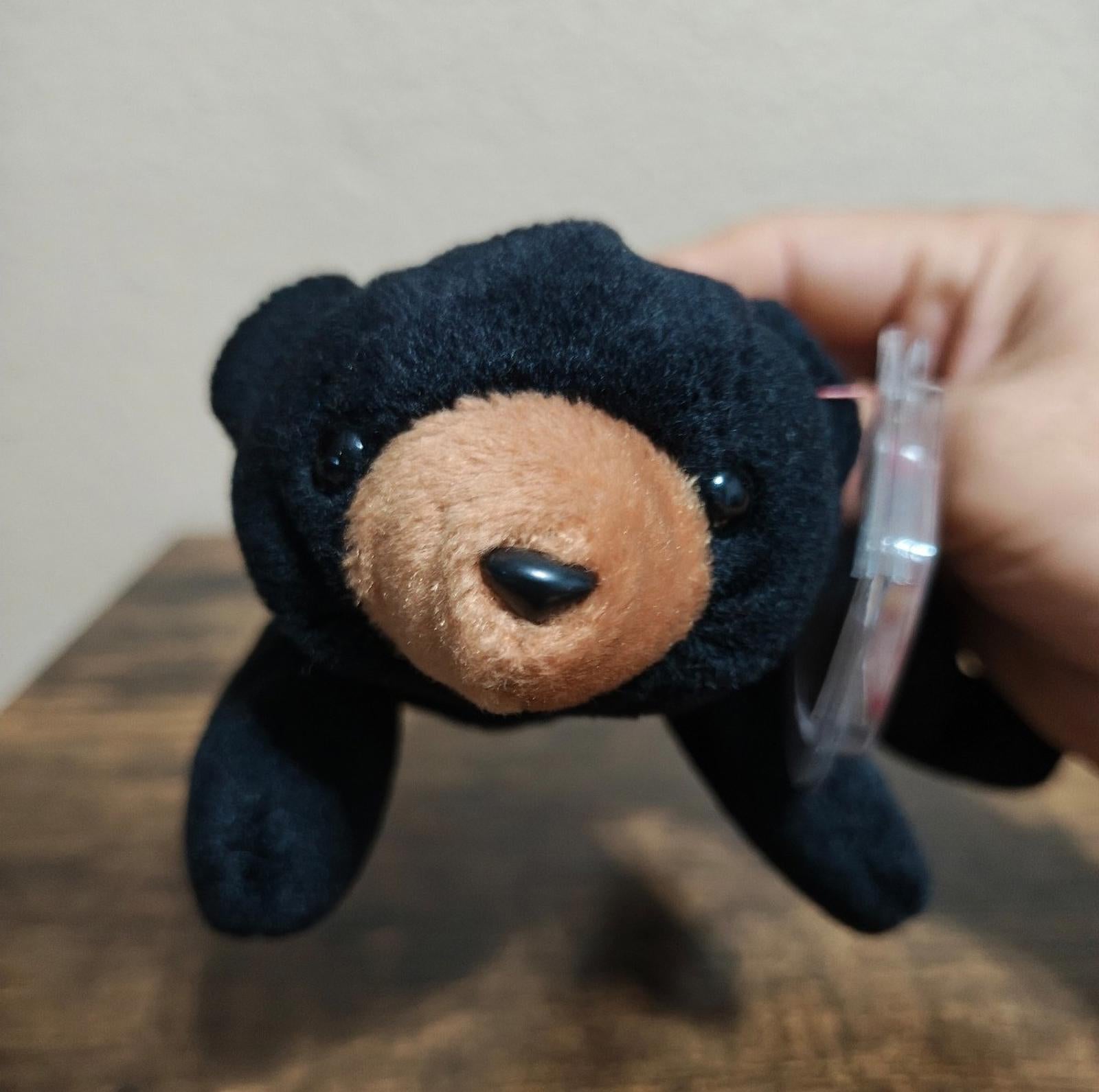 Black plush bear beanbag with tan snout and embroidered eyes, lying on wooden table