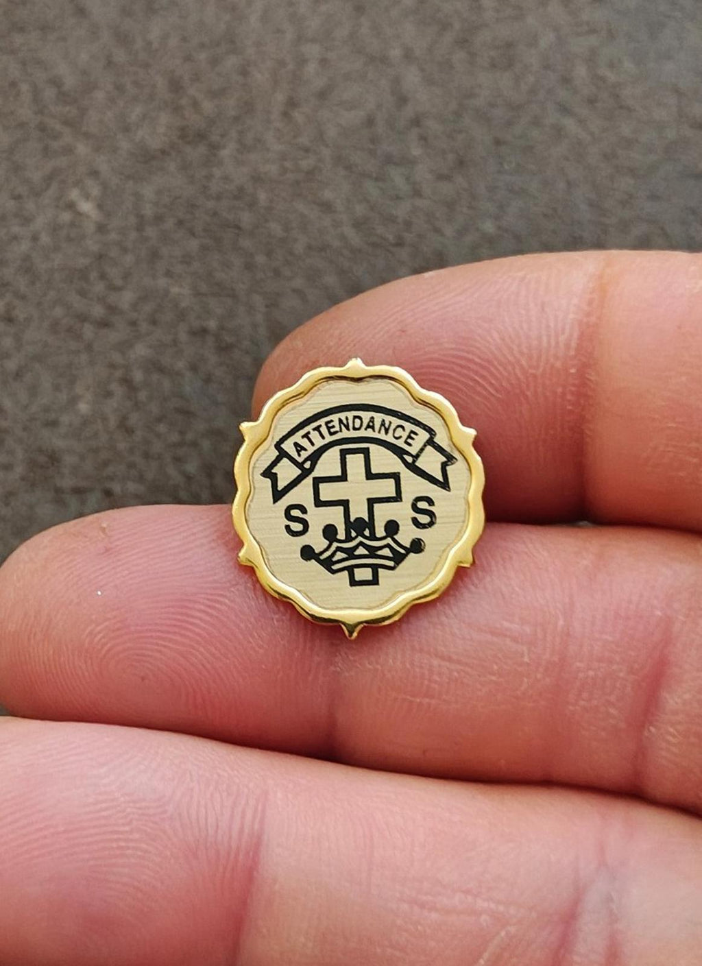 Gold-tone attendance badge pin with cross, banner reading "ATTENDANCE", and S letters.