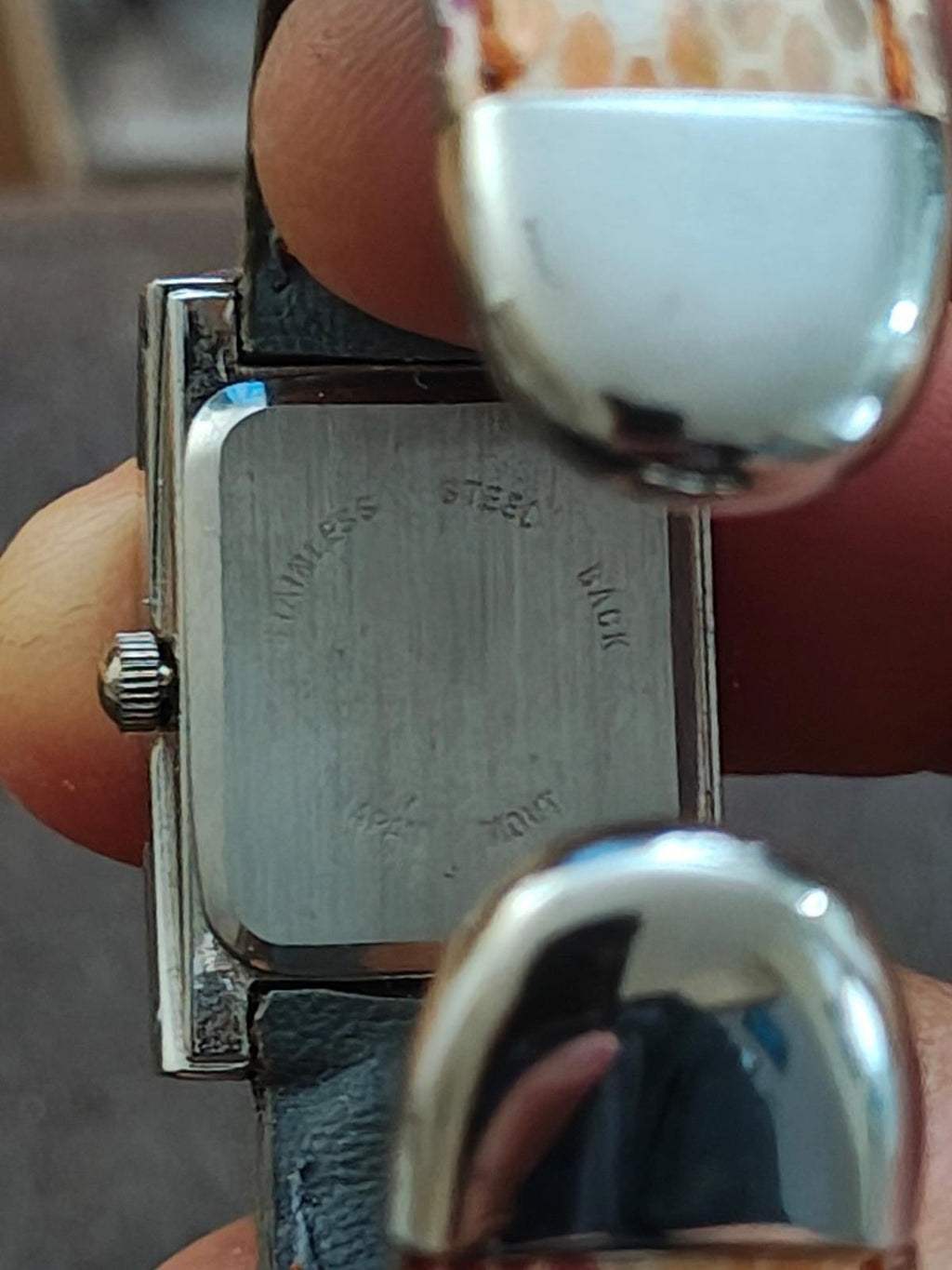 Metal case back of square cuff watch with engraved markings and clasp