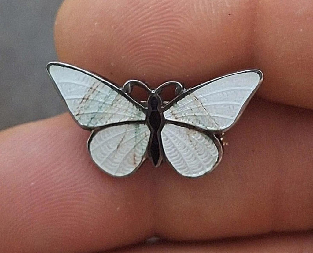 Enamel butterfly pin brooch with white wings and dark body, close-up on finger.