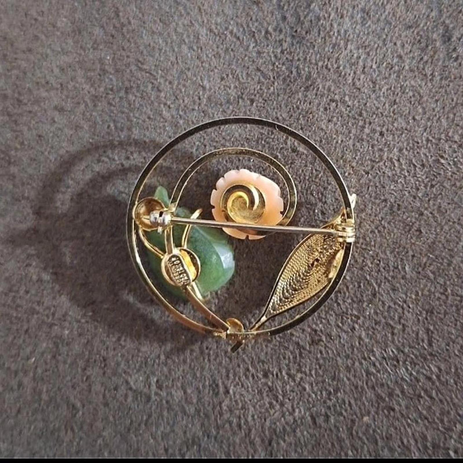 Gold-tone brooch viewed from an angle, showing pale rose and green leaves behind.