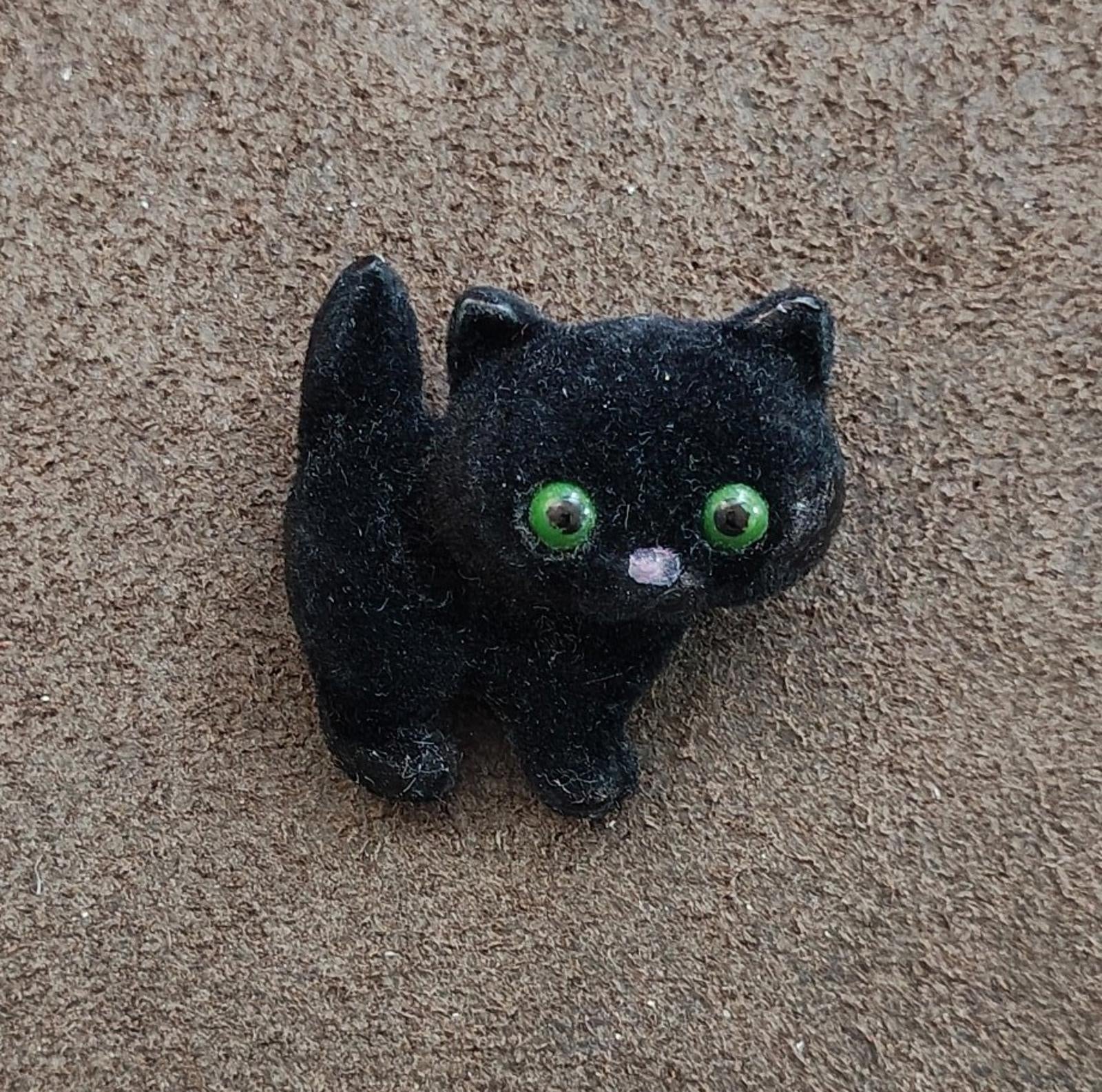 Black fuzzy cat brooch with green eyes and small white nose