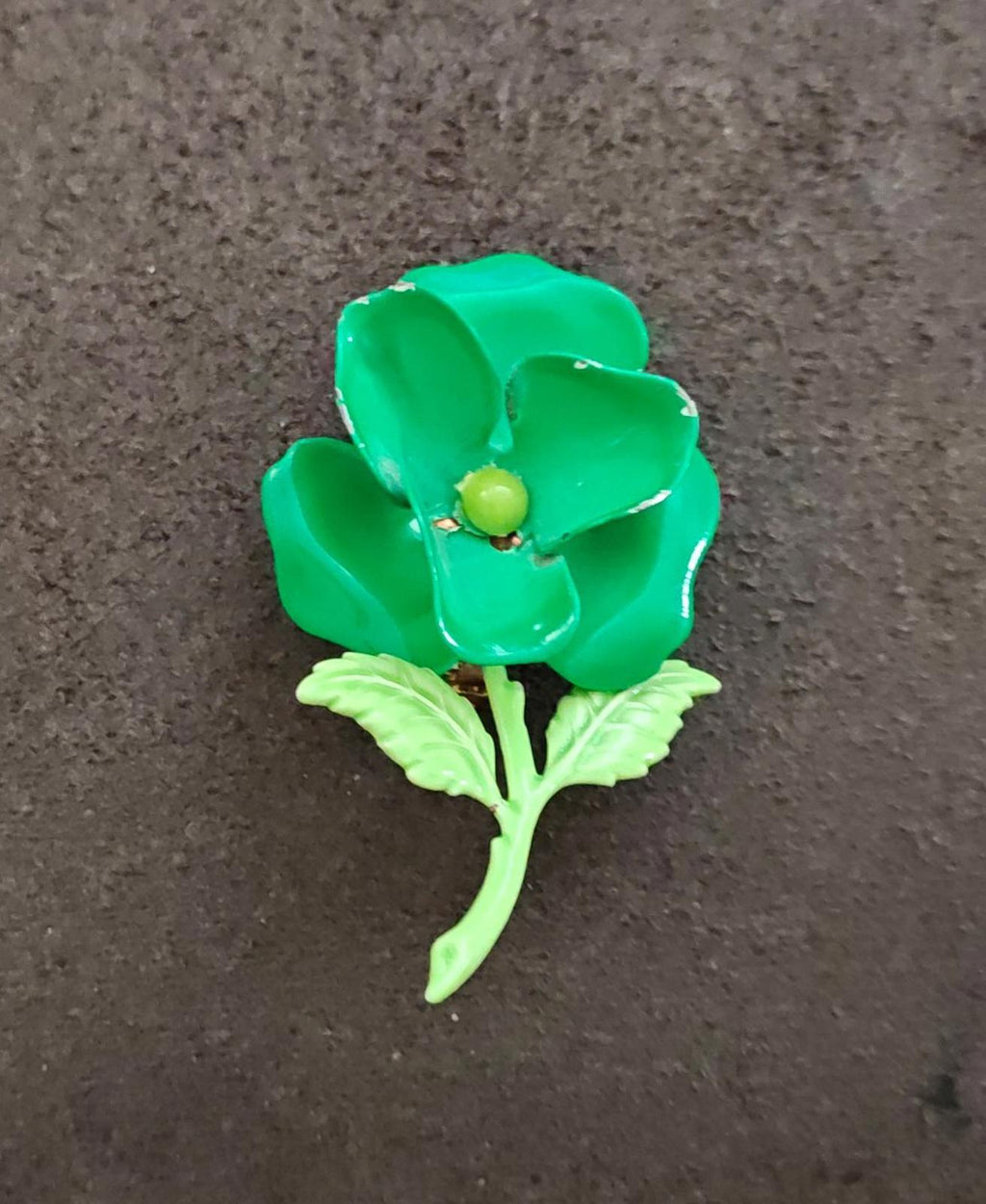 Green enamel flower brooch with gold center bead and leaf stems, angled view.