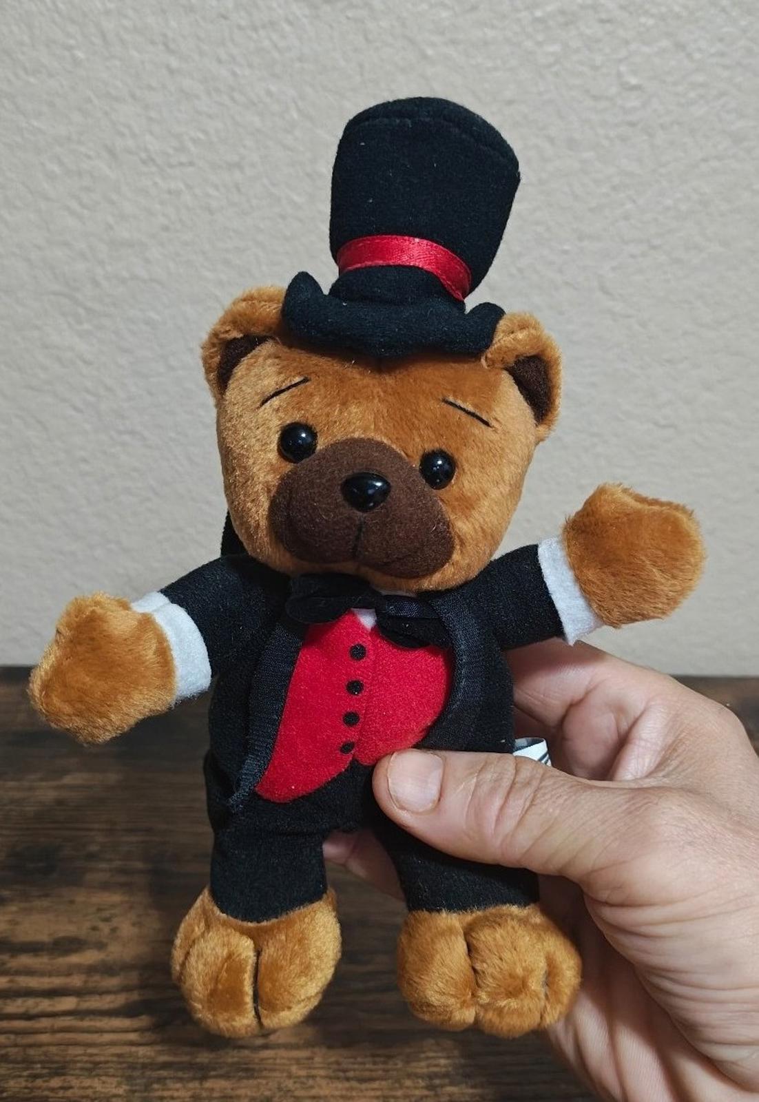 Brown plush bear in black tuxedo, red vest, and tall top hat with red band.