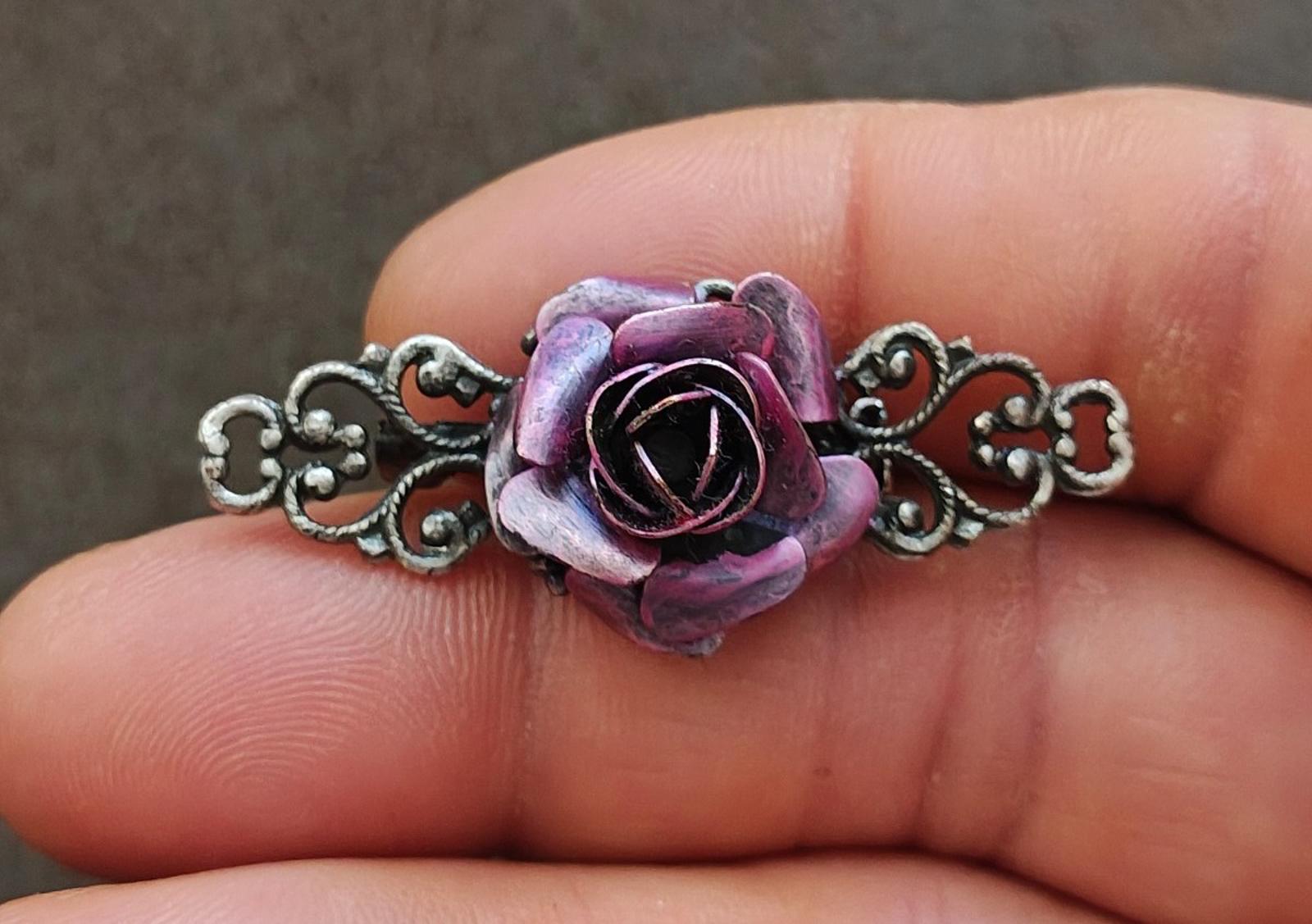 Silver tone filigree brooch with purple rose and dark center detail, held in hand