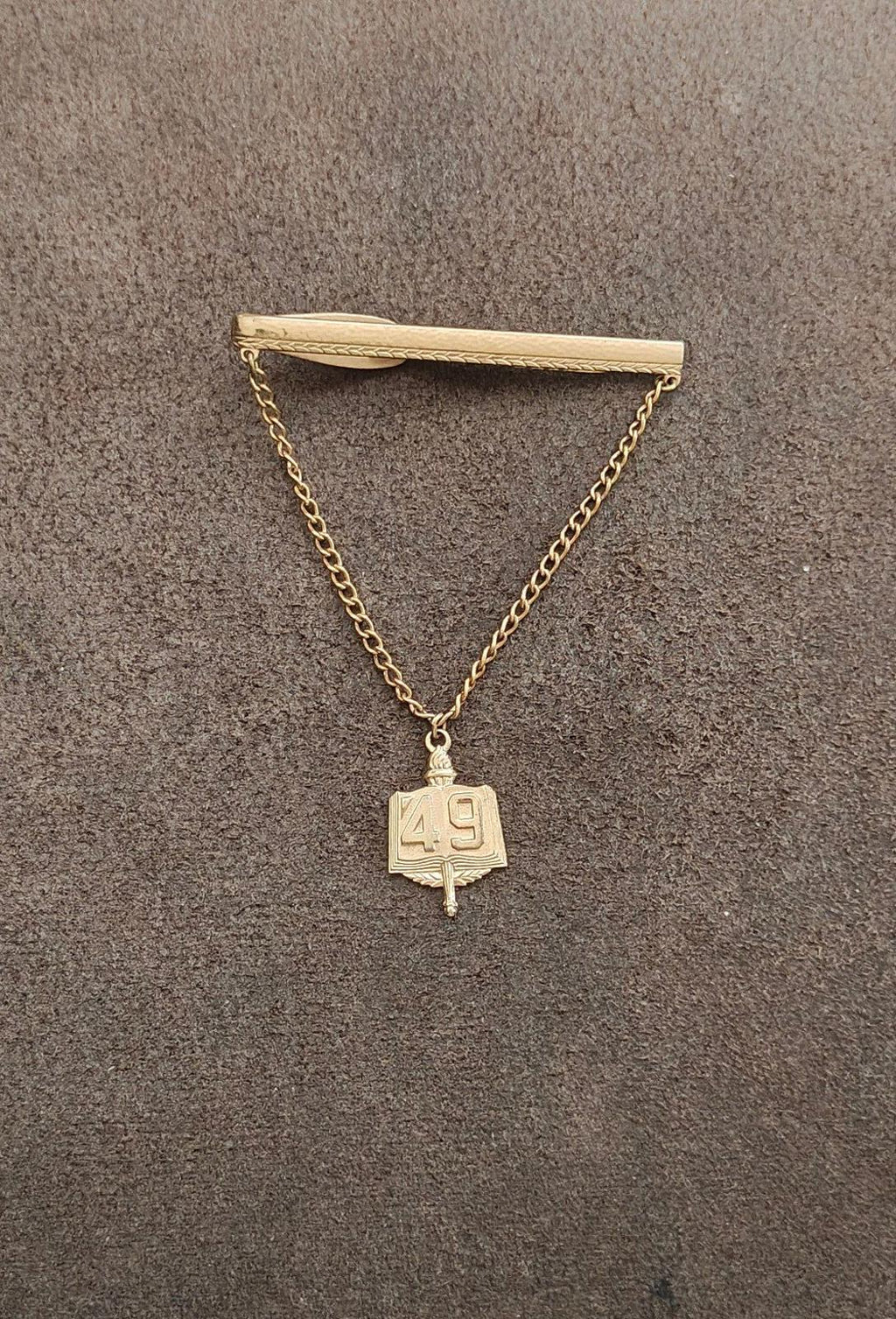 Gold-tone tie clip with hanging book charm marked 49 and long chain