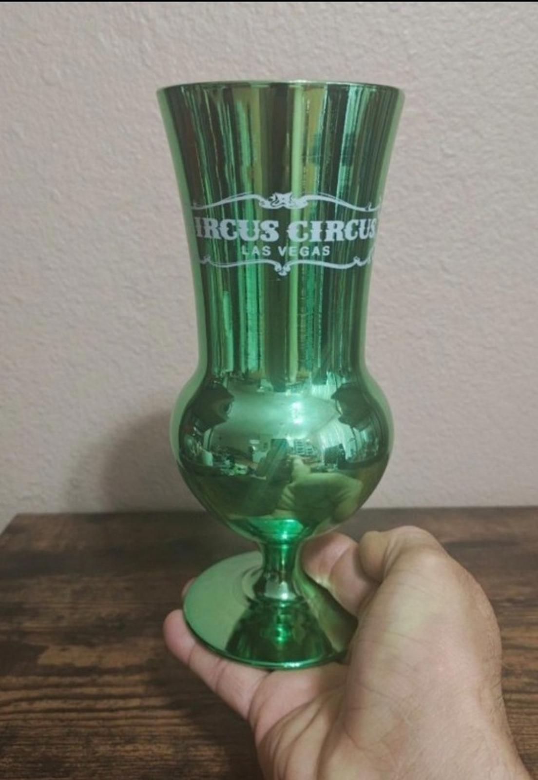 Green mirrored hurricane glass held in hand, flared top and rounded base.
