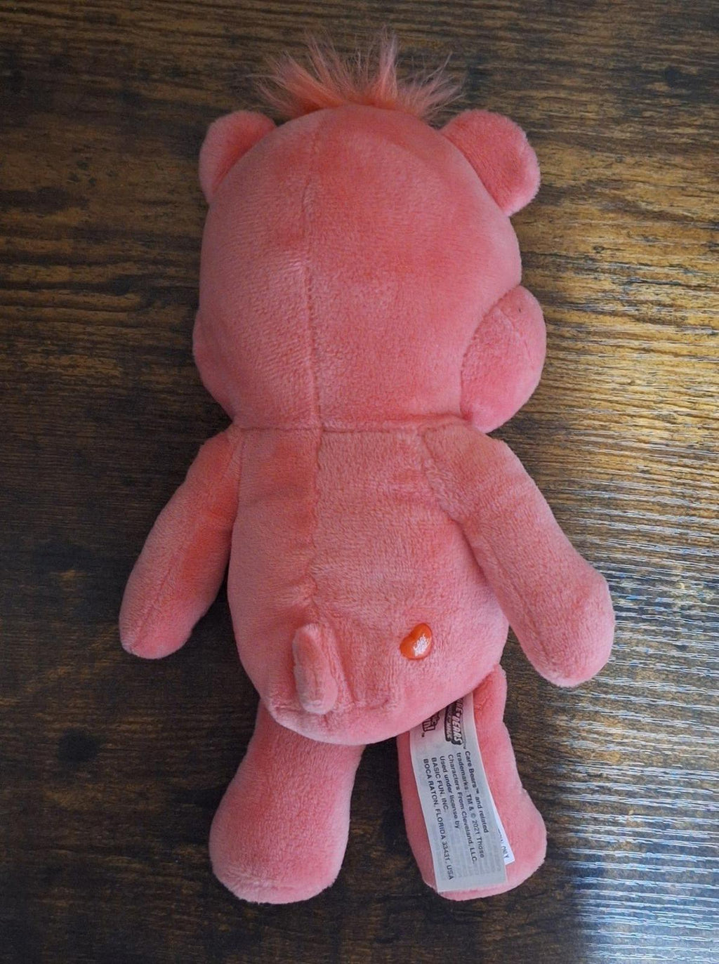 Pink plush bear back view on wooden surface with tag at the bottom