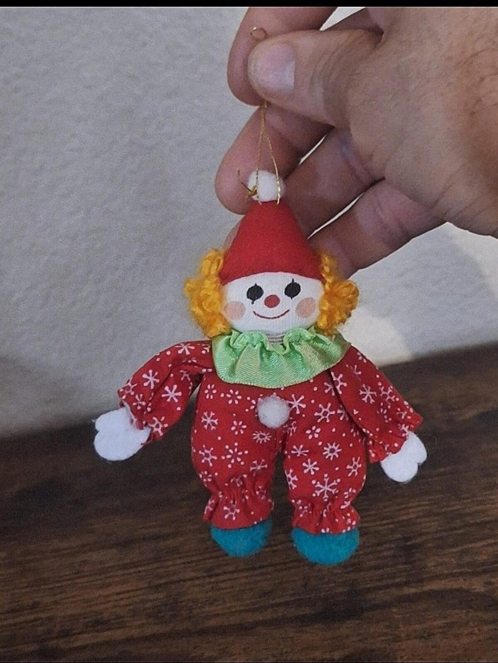 Hand holding a soft stuffed clown ornament in red snowflake outfit with green ruffle and hanging loop