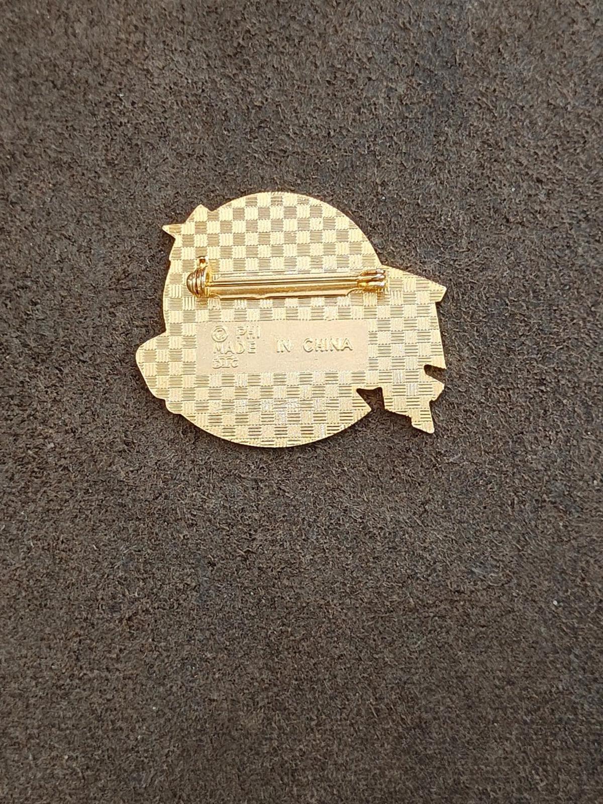 Gold-tone pin back with hinge clasp and textured pattern, no front text.