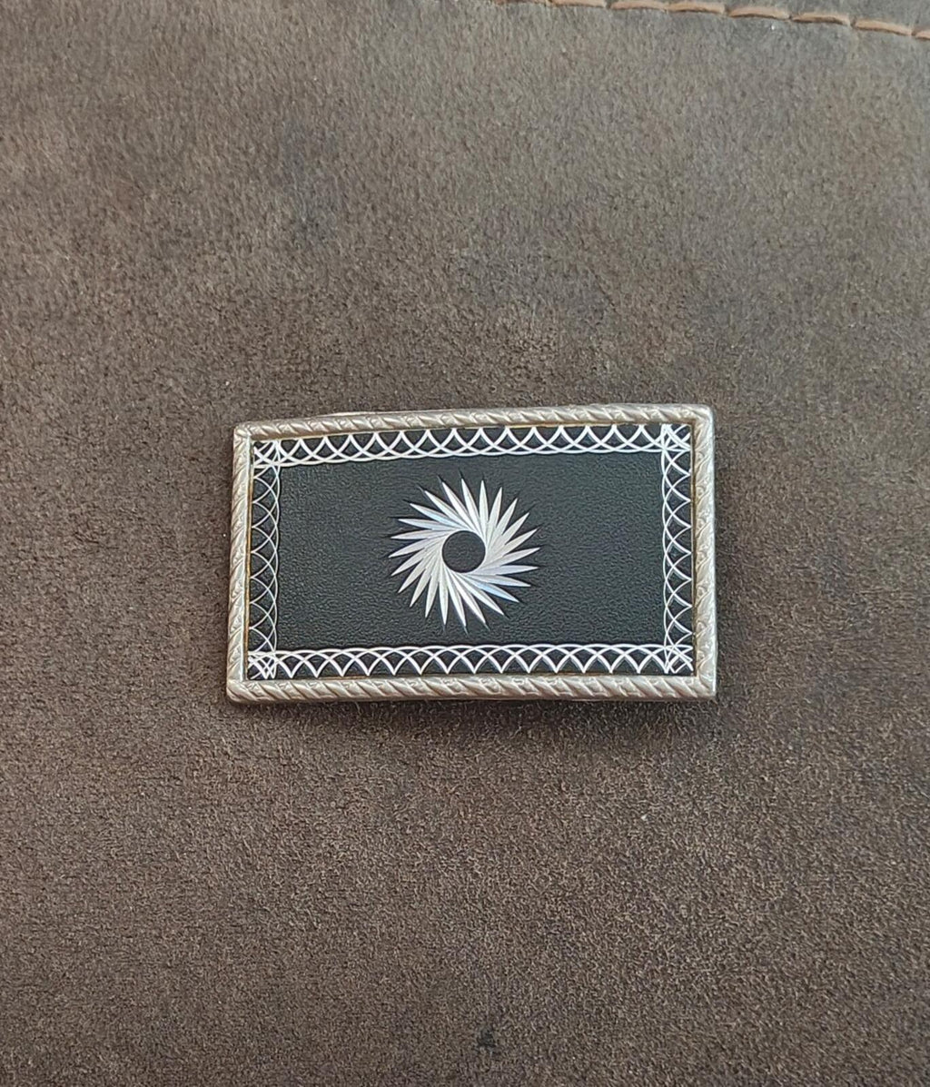 Western belt buckle close-up: silver starburst etched in black rectangle