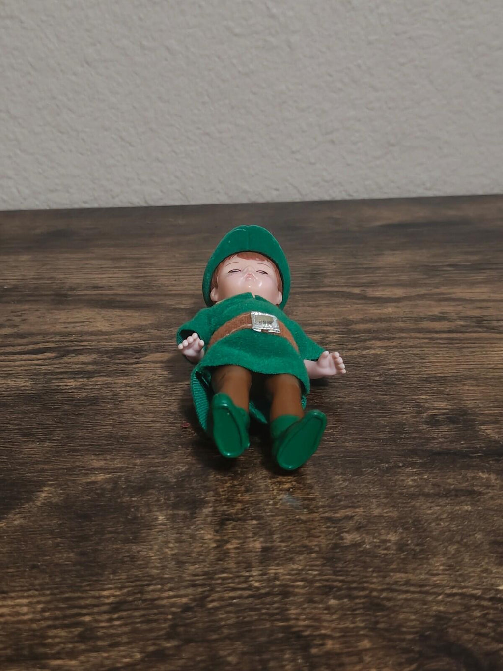 Collectible doll lying on its back wearing green hat, tunic, gold belt, and boots