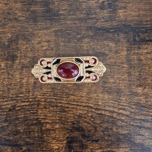 Gold-tone oval bar brooch with red lucite center cabochon and scrollwork sides