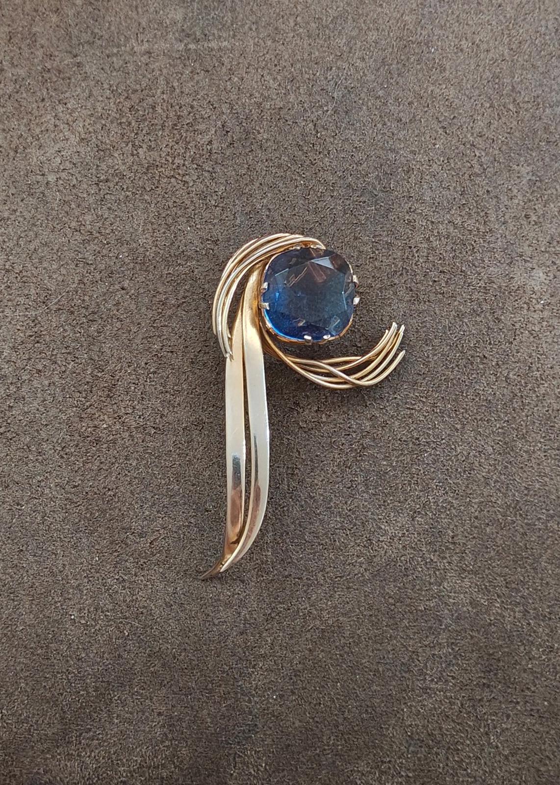 Gold-tone abstract brooch pin with large blue gemstone and flowing curved element