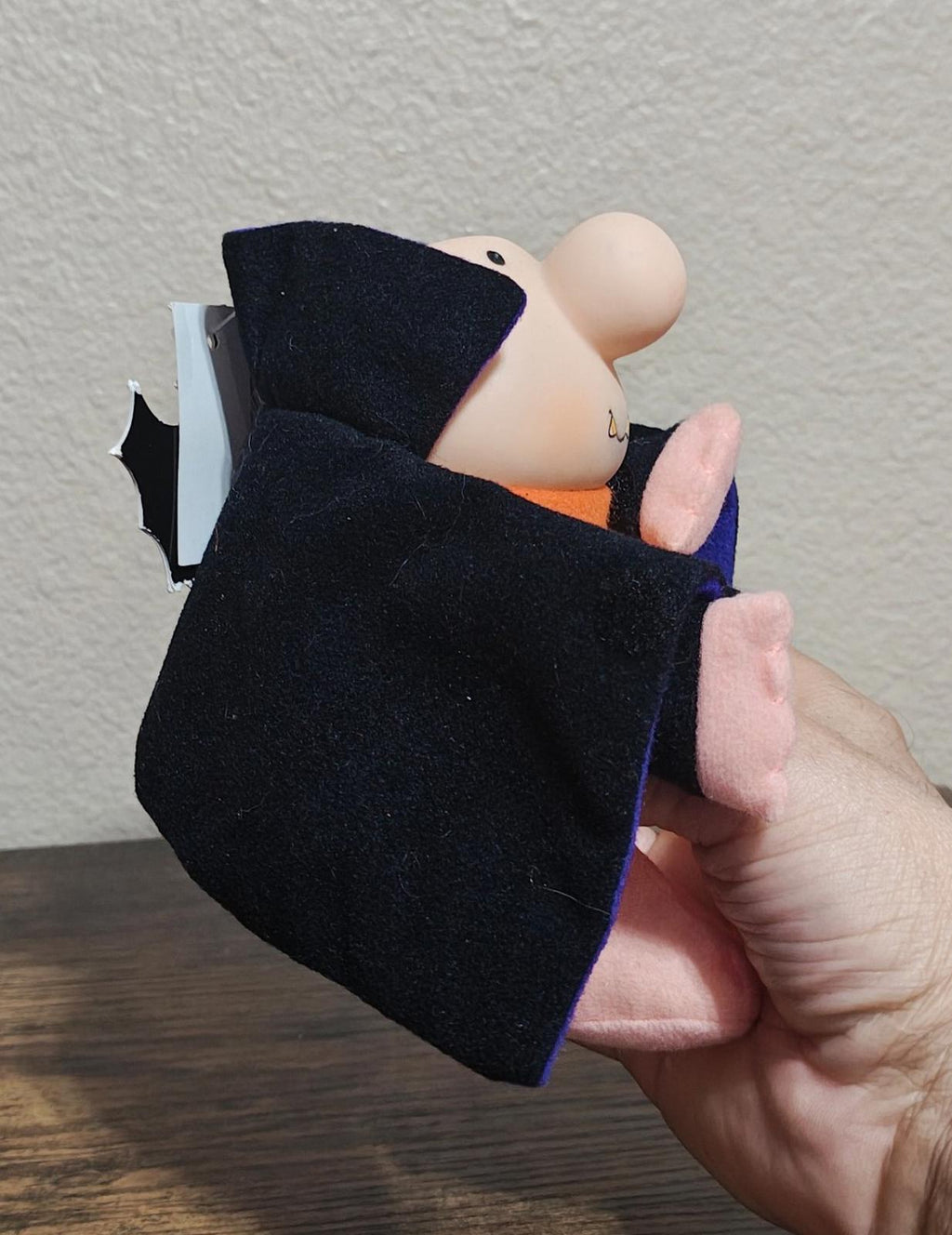 Side view of Dracula plush in dark cape with purple lining, pink hands and feet