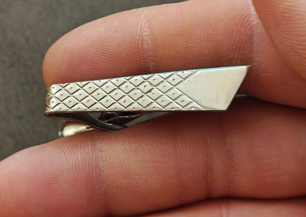 Silver-tone geometric tie bar clip with textured diamond pattern and angled end