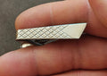 Silver-tone geometric tie bar clip with textured diamond pattern and angled end