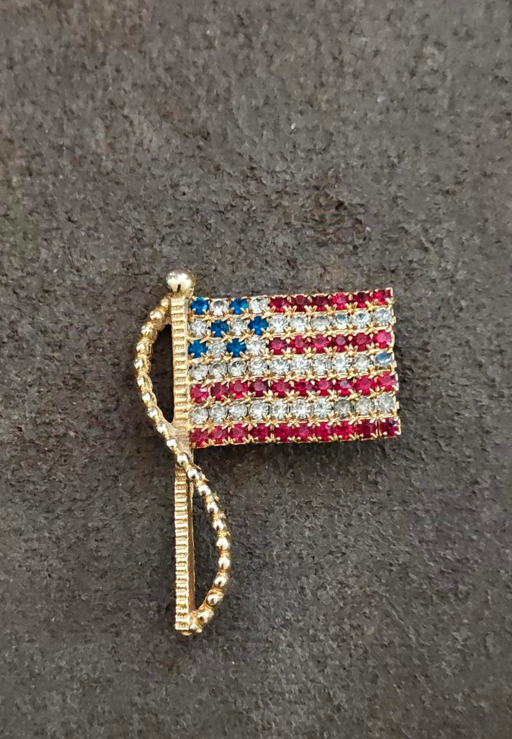 Gold-tone American flag rhinestone pin brooch on tabletop, angled