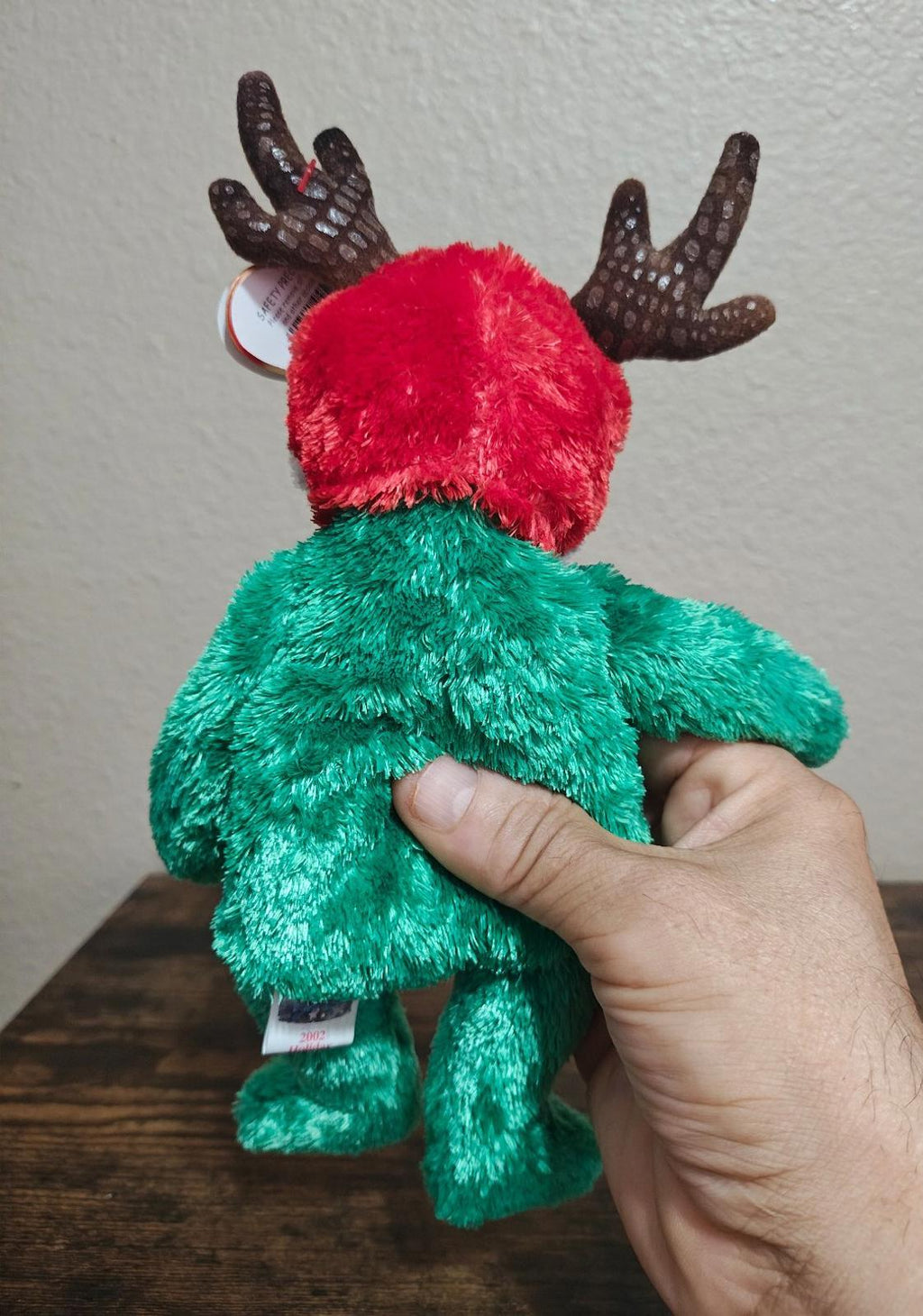 Green plush reindeer teddy bear with red-and-white back hat and antlers