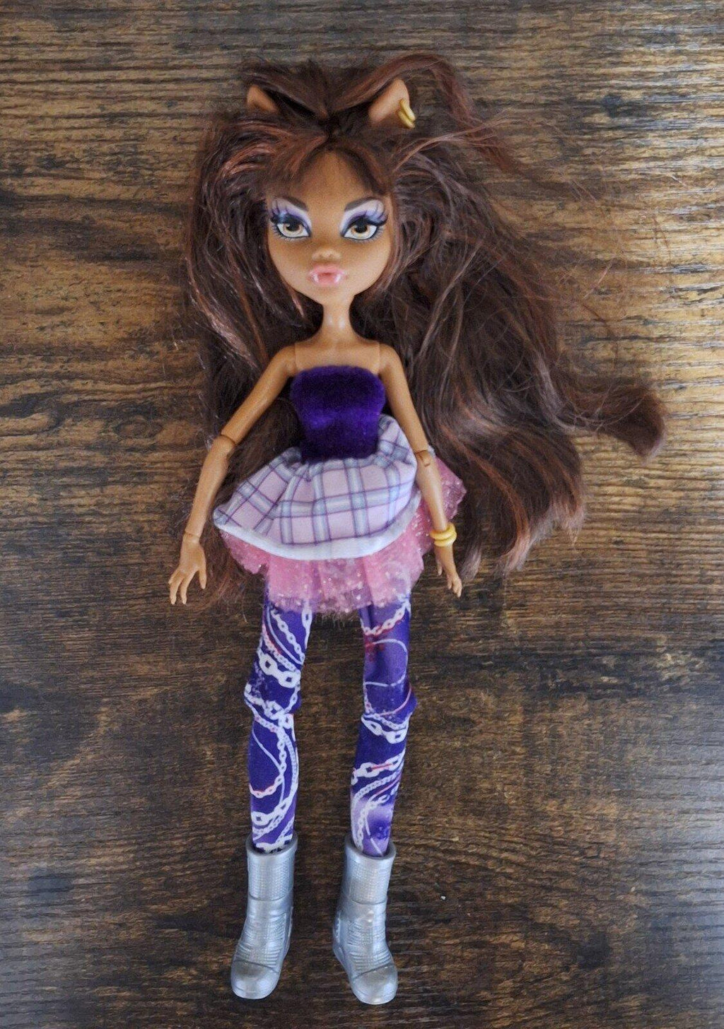 Fashion doll standing wearing purple glitter top, plaid skirt, and patterned purple pants