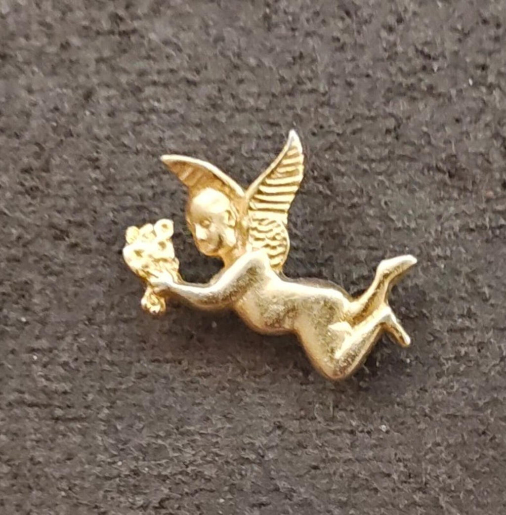 Gold tone flying angel brooch holding flowers, close-up on fabric