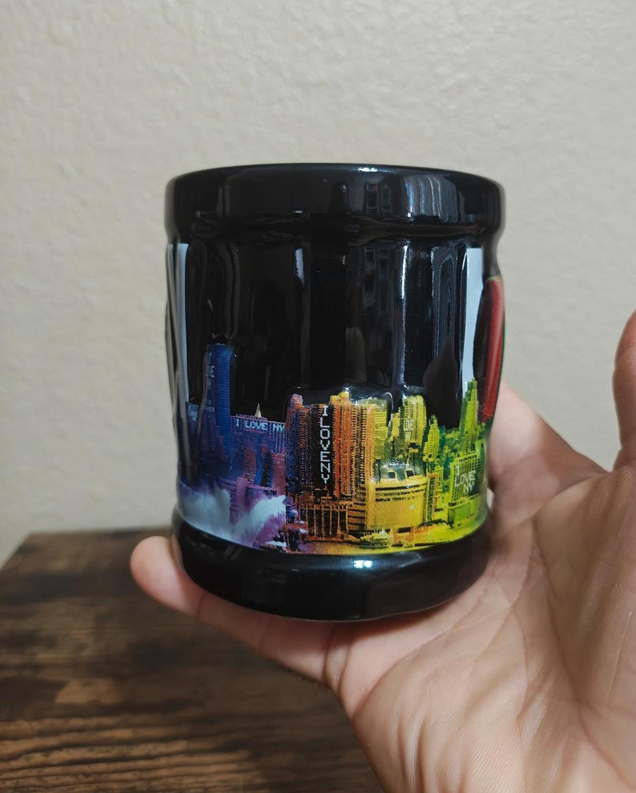 Black ceramic mug with colorful skyline graphic band, glossy glaze, held in hand