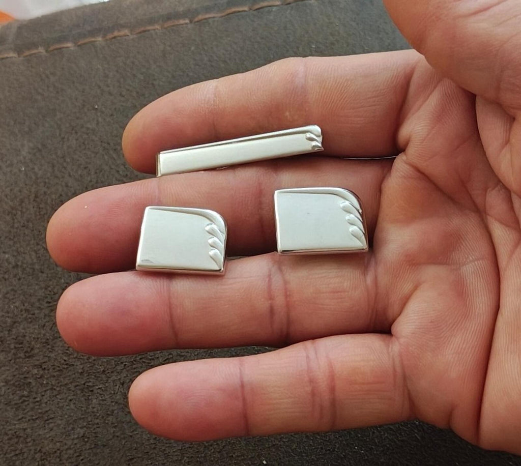 Silver tie bar and cufflinks set in hand; rectangular faces with raised art-deco ridges