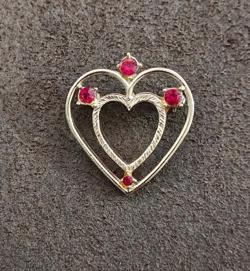 Heart-shaped gold-tone brooch with red rhinestone stones, centered front design