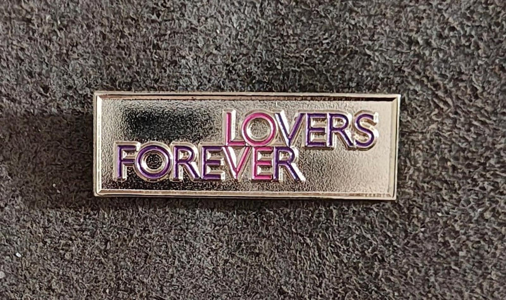 Gold-tone “Lovers Forever” enamel pin, rectangular border with stacked “LOVERS” and “FOREVER”.