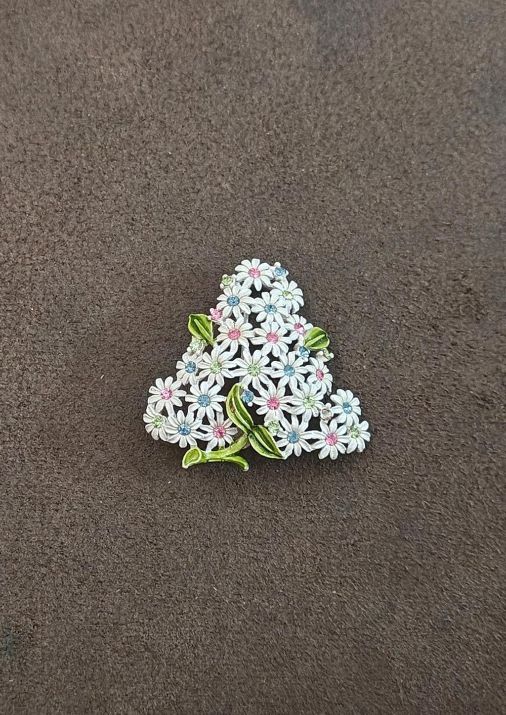 Gold-tone floral rhinestone brooch with white petals, blue highlights, pink centers, and green leaves