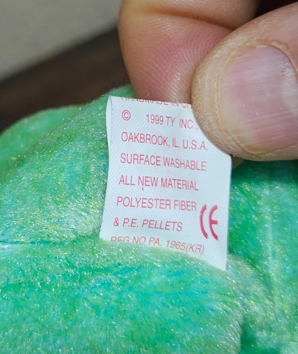 White fabric label on green plush with care and material text.