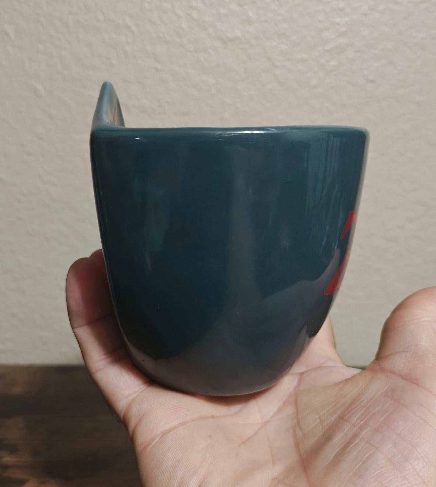 Blue ceramic mug, back view with partial shield logo visible on the right.