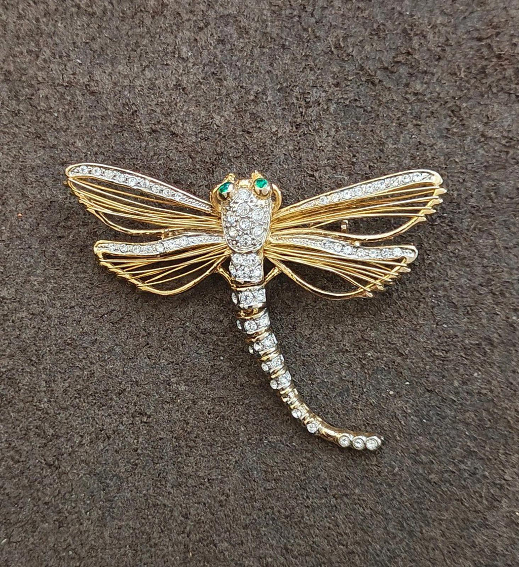 Gold-tone dragonfly rhinestone pin with green enamel eyes, full view on dark surface